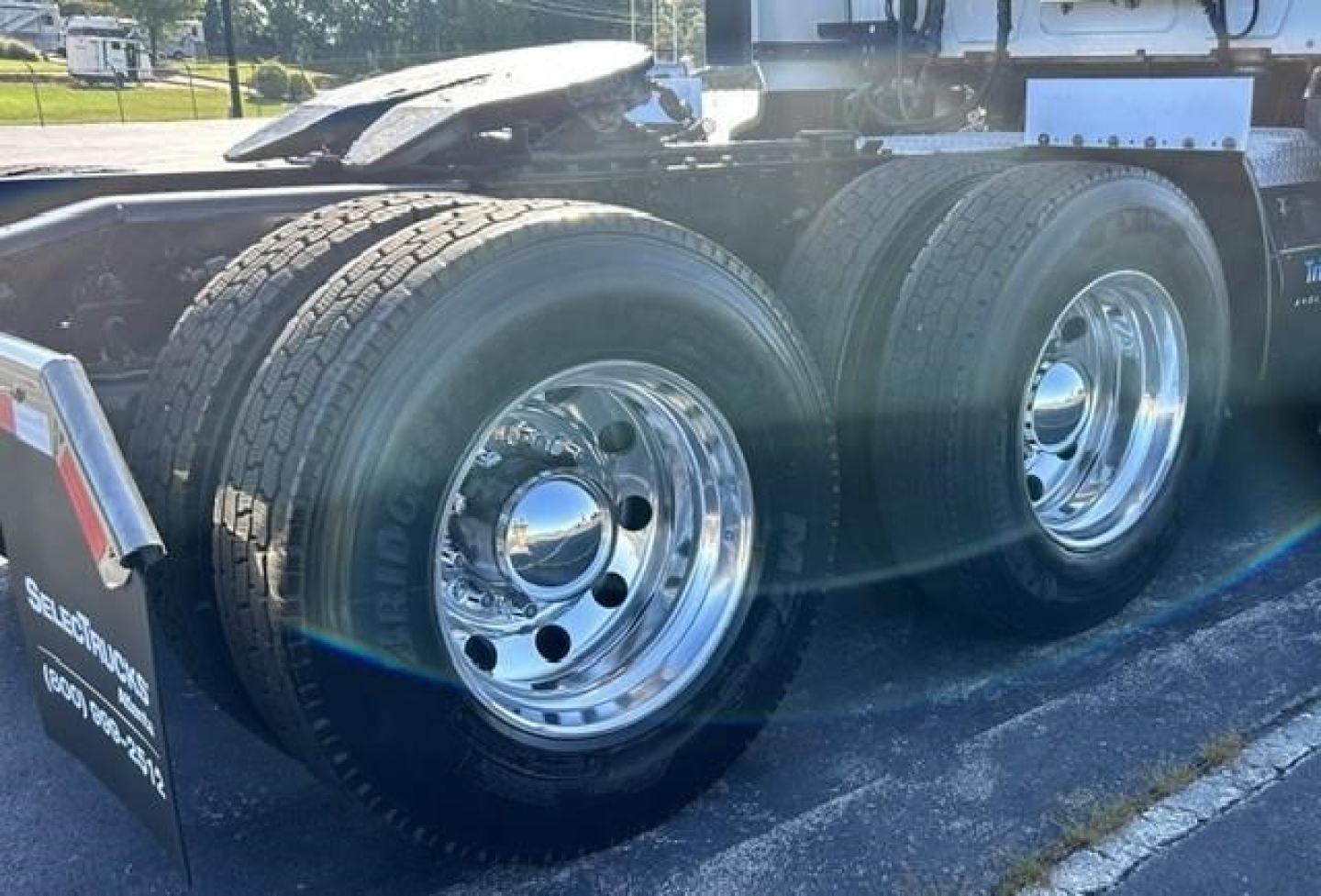 Dual rear axles of a semi-truck trailer showing shiny chrome wheels and heavy-duty tires, with fender and mud flaps visible.