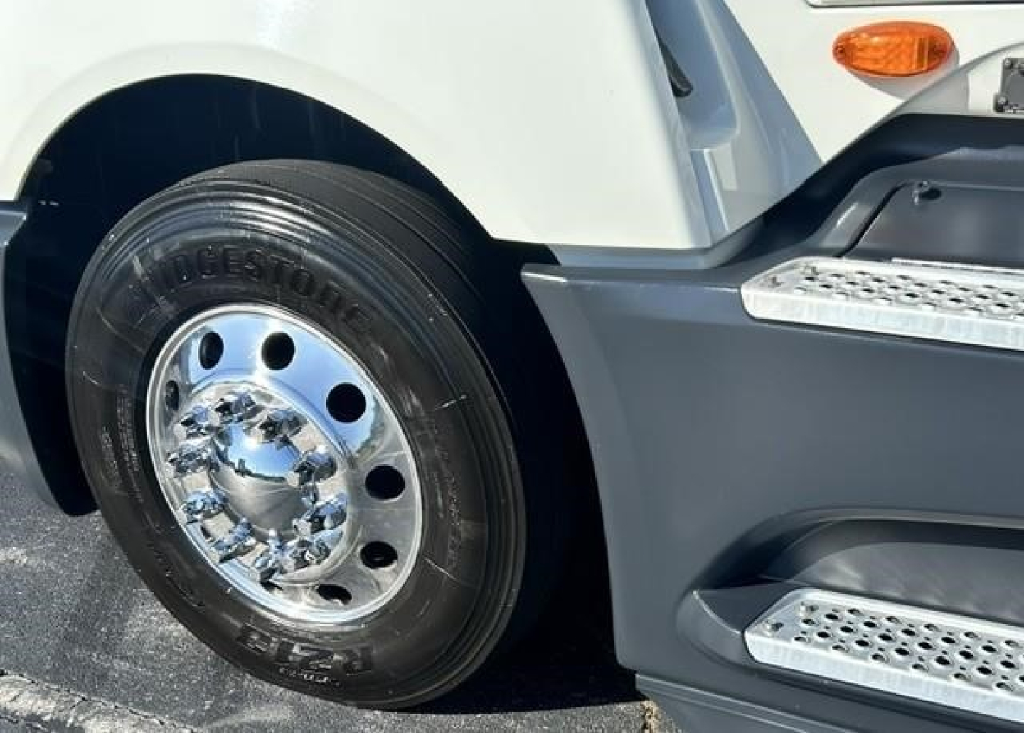Truck wheel and front fender of a 2021 International LT with a polished chrome hubcap and tire, part of the front sleeper area visible.