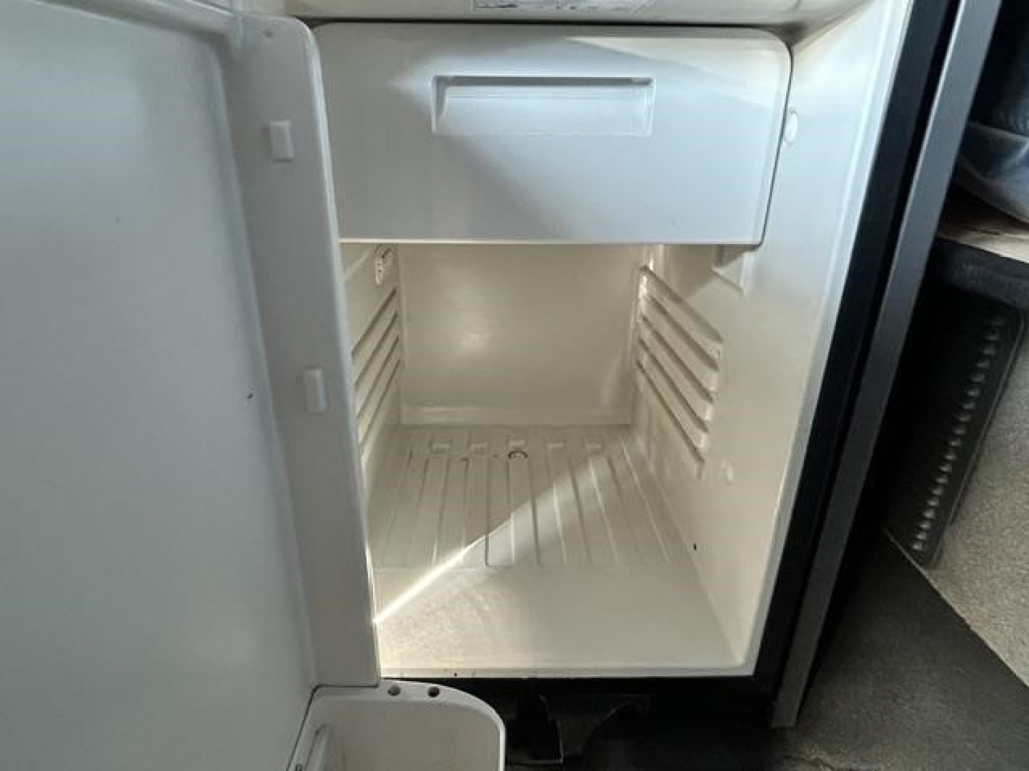 Mini fridge/freezer in a truck cab with empty interior and side shelves.
