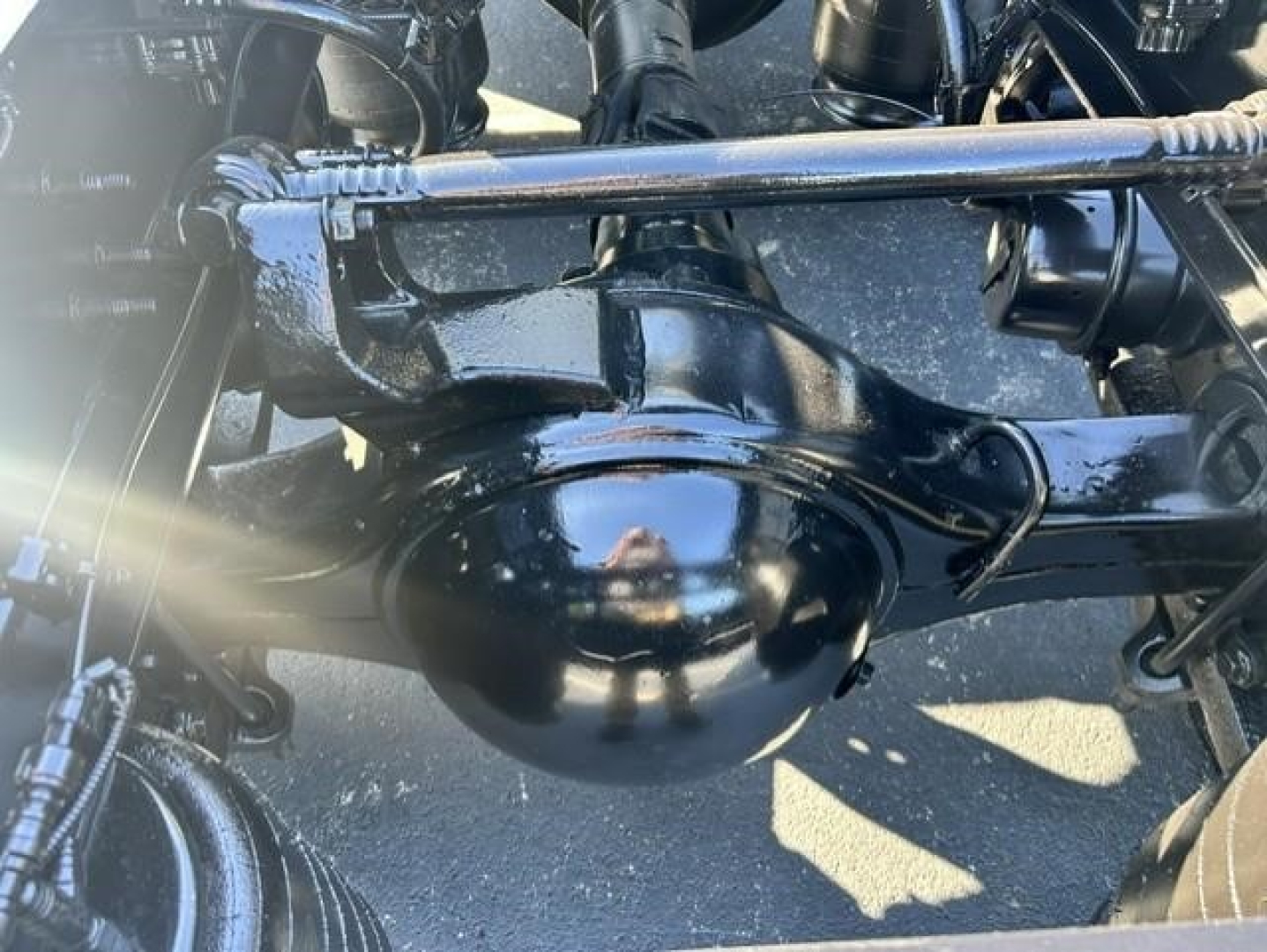 Rear view of truck suspension and differential housing with black paint and glossy finish, visible drive axle, leaf springs, and surrounding components.
