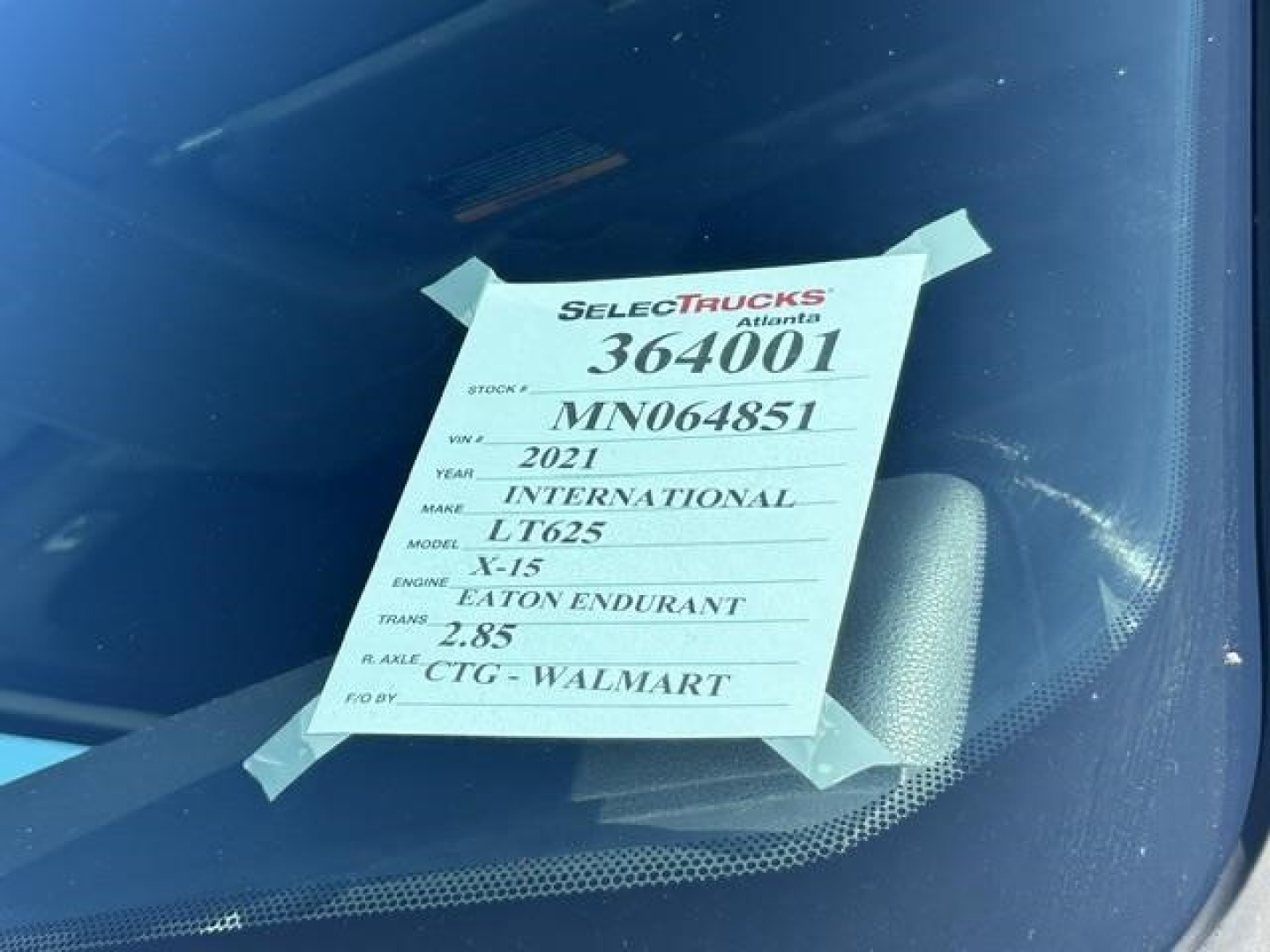 Label on windshield with truck details: Stock 364001, VIN MN064851, year 2021, make International, model LT625, engine X-15, transmission Eaton Fuller, ROE 2.85, CTG Walmart.
