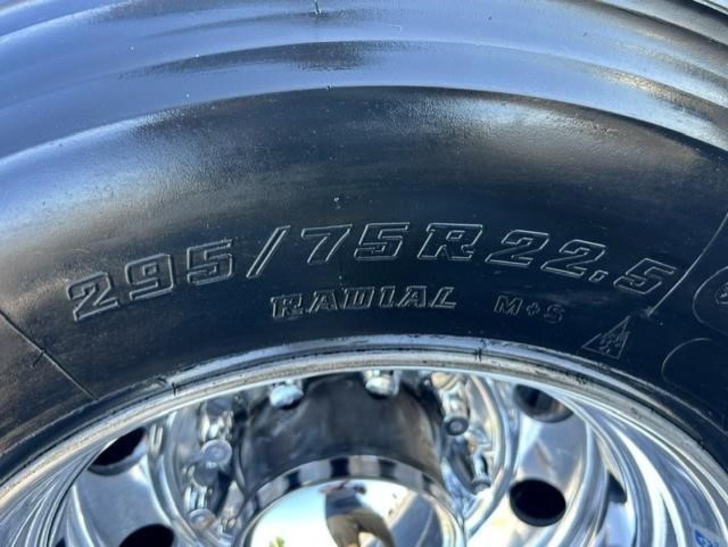 Tire close-up showing size 295/75R22.5 radial equipped on chrome wheel, part of a truck.