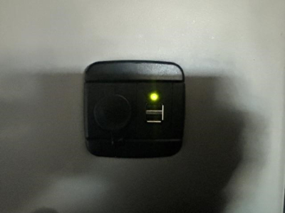 Small black 12V auxiliary power port with a green LED indicator and a USB port visible on a metal surface.