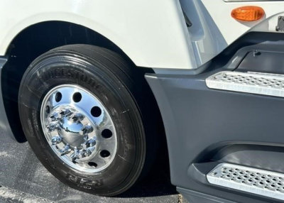Truck wheel and front fender of a 2021 International LT with a polished chrome hubcap and tire, part of the front sleeper area visible.
