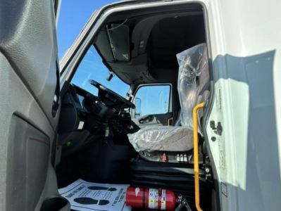 Interior of a used 2021 International LT sleeper cab showing driver seat, steering wheel, dashboard, and plastic-wrapped seat; visible fire extinguisher on floor; cab entry with yellow grab bar.