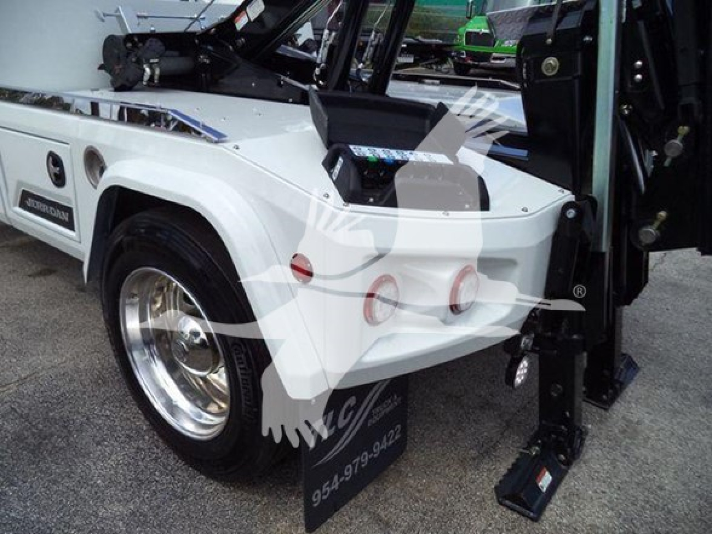 International MV winch truck rear quarter showing white body, chrome wheel, blue accent, and hydraulic winch controls on bed with black step/ladder near fender.