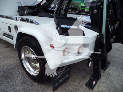International MV winch truck rear quarter showing white body, chrome wheel, blue accent, and hydraulic winch controls on bed with black step/ladder near fender.