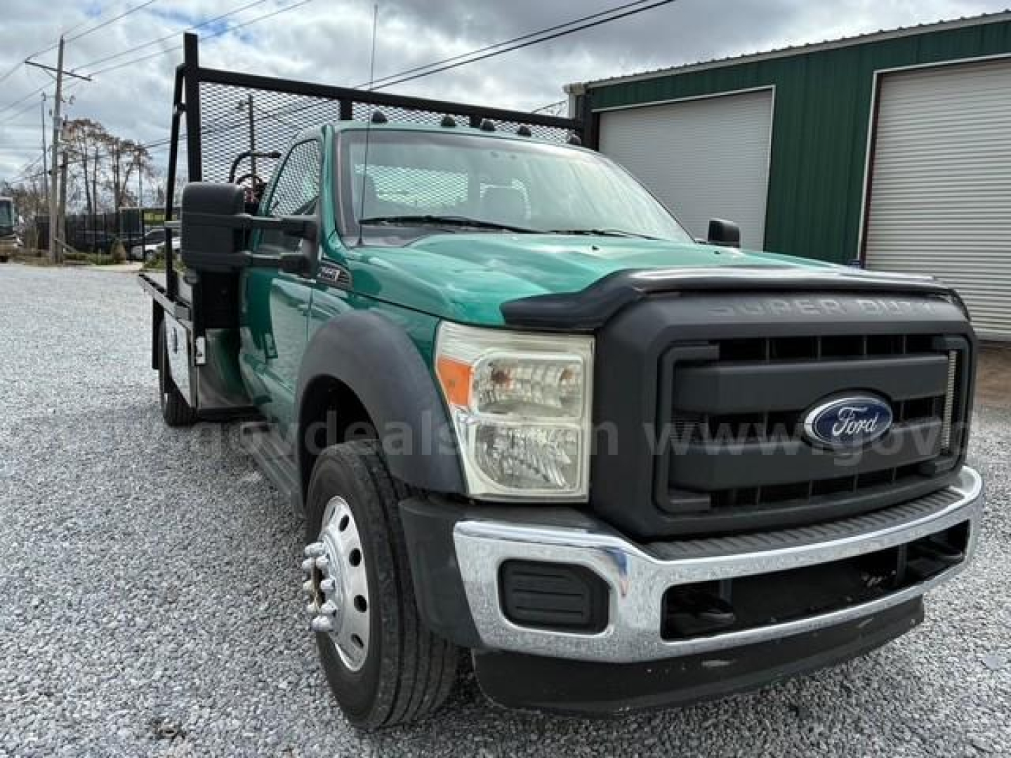 Ford F-550 flatbed truck viewed from front-left, green cab, black grille, chrome bumper, dual rear wheels, flatbed with side rails.