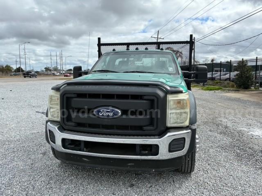 Front view of a 2012 Ford F-550 flatbed truck with black grille, Ford emblem, and large bumper in a gravel lot.