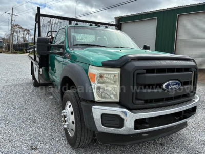 Ford F-550 flatbed truck viewed from front-left, green cab, black grille, chrome bumper, dual rear wheels, flatbed with side rails.