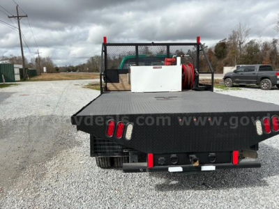 Flatbed truck rear view showing flatbed with metal diamond plate, built-in tool/storage, spare hose reel, and taillights.