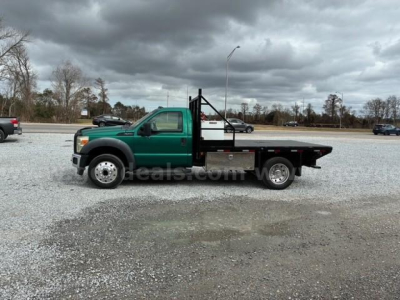 Flatbed tow truck side view 2012 Ford F-550 with green cab and black flatbed showing wheel and deck details.