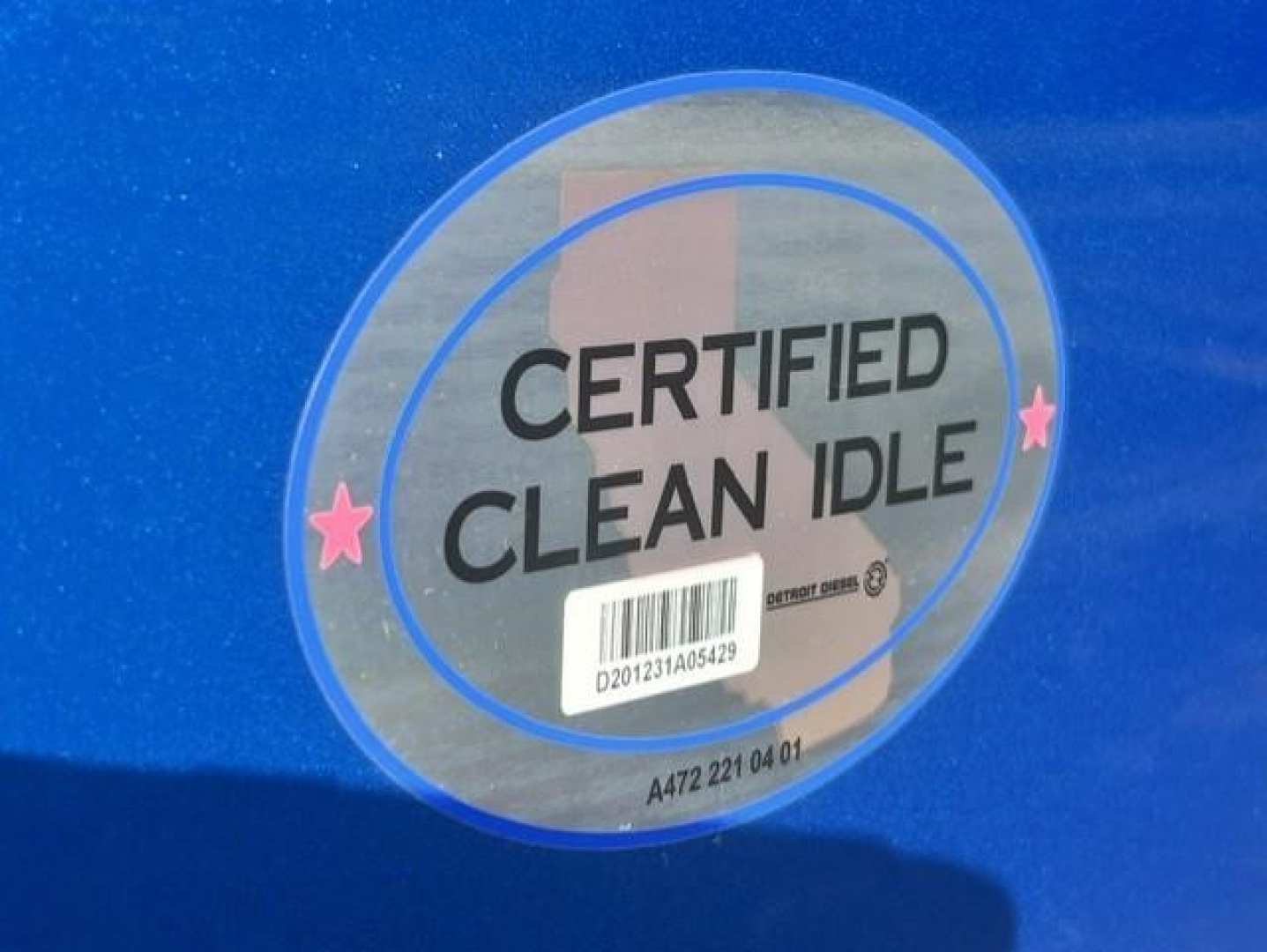 Label on blue Freightliner truck indicating CERTIFIED CLEAN IDLE with barcode and small pink stars.
