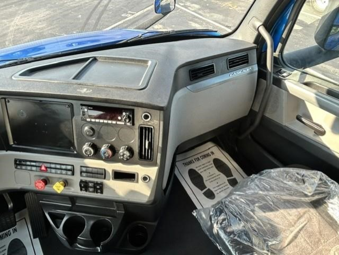 Dashboard and cockpit of a Freightliner Cascadia 126 truck interior with center touchscreen, climate controls, and steering wheel visible.