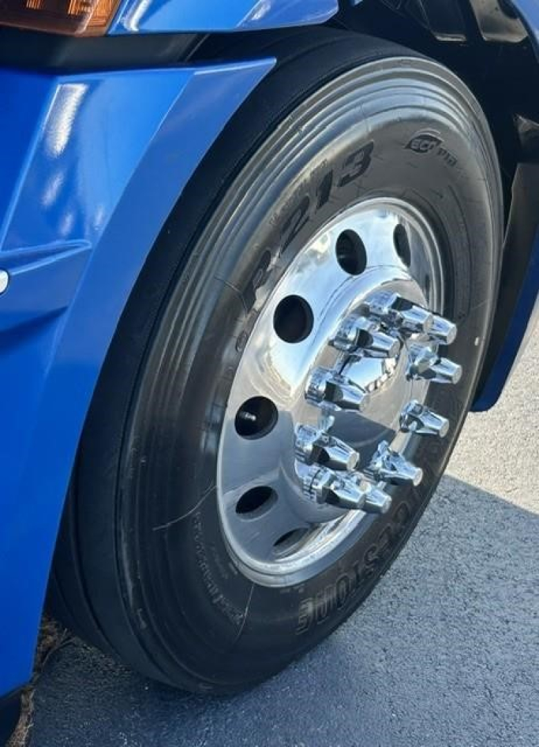 Blue Freightliner Cascadia 126 front wheel and tire close-up showing large dual axle hub with chrome lug nuts.