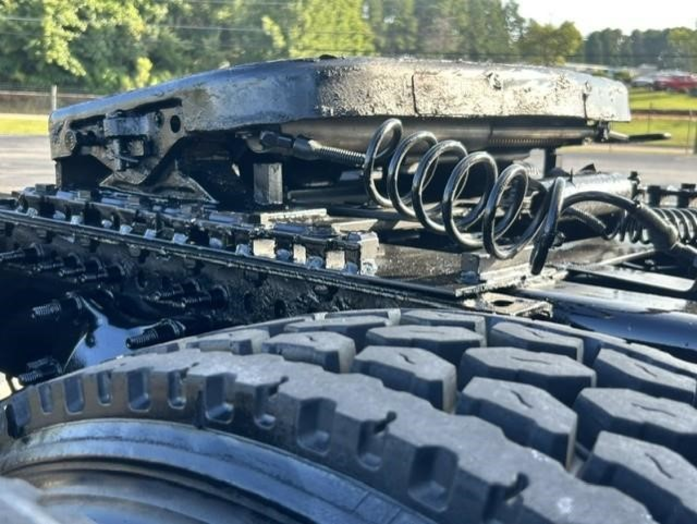 Truck rear section showing suspension components, coil springs, and exposed wiring near the fifth wheel, with heavy-duty tires in foreground.