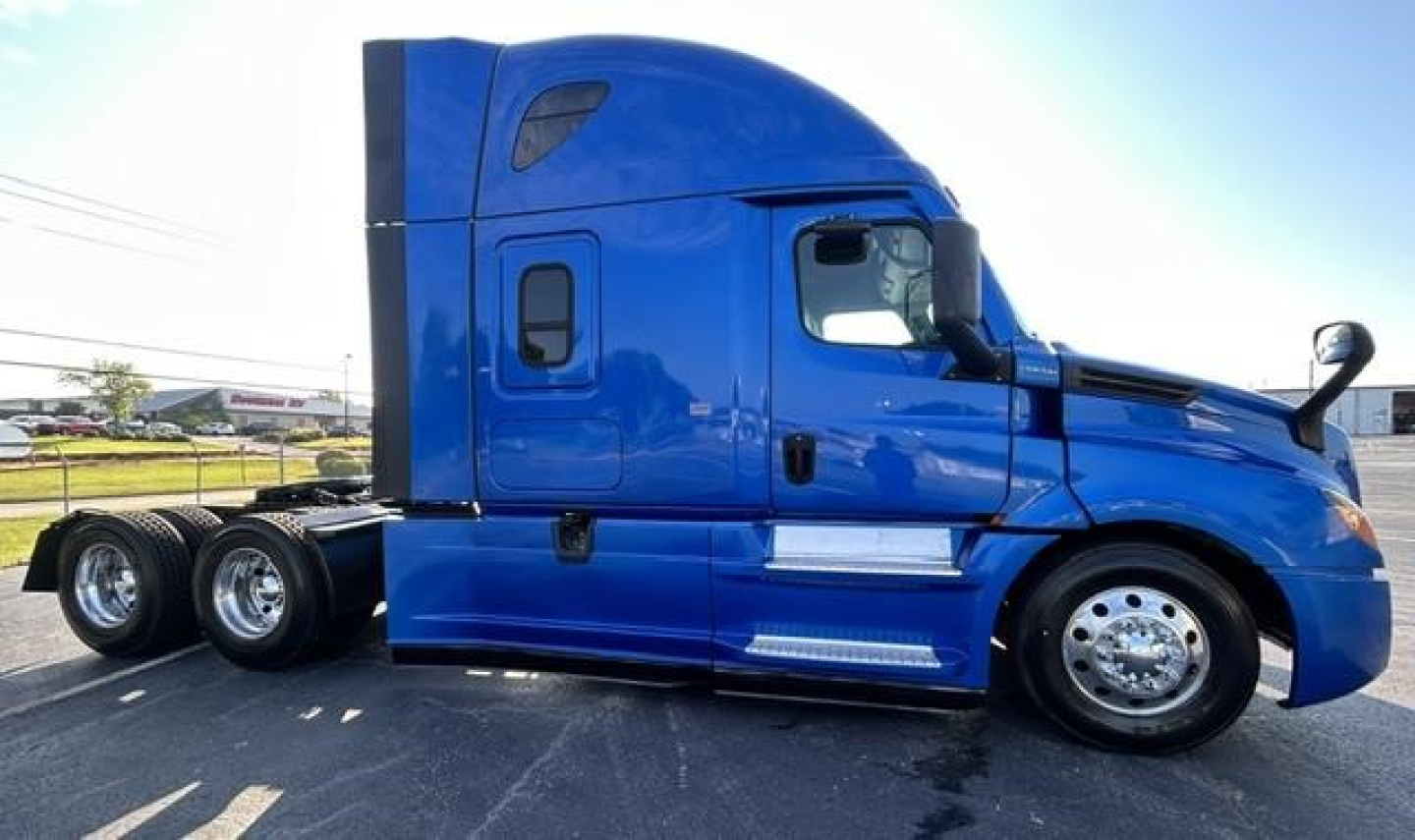 Truck side profile showing a blue 2022 Freightliner Cascadia 126 sleeper cab with triple rear axles and chrome wheels.