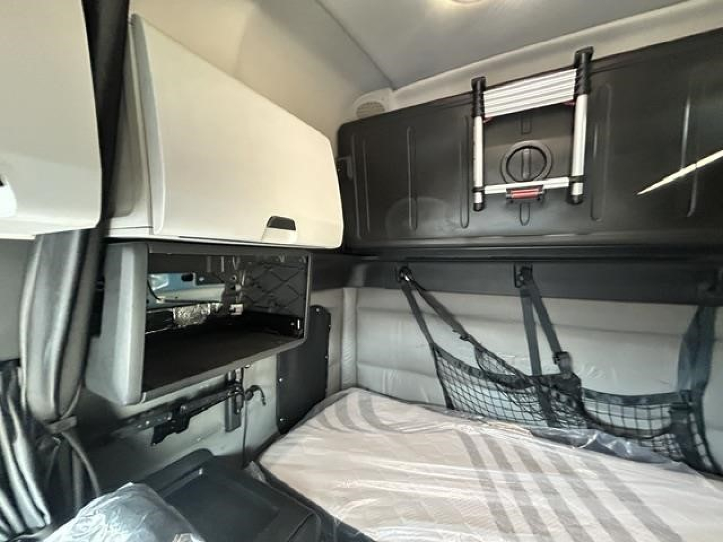 Freightliner Cascadia 126 sleeper cab interior showing bunk area with storage compartments, netting, and overhead compartments.