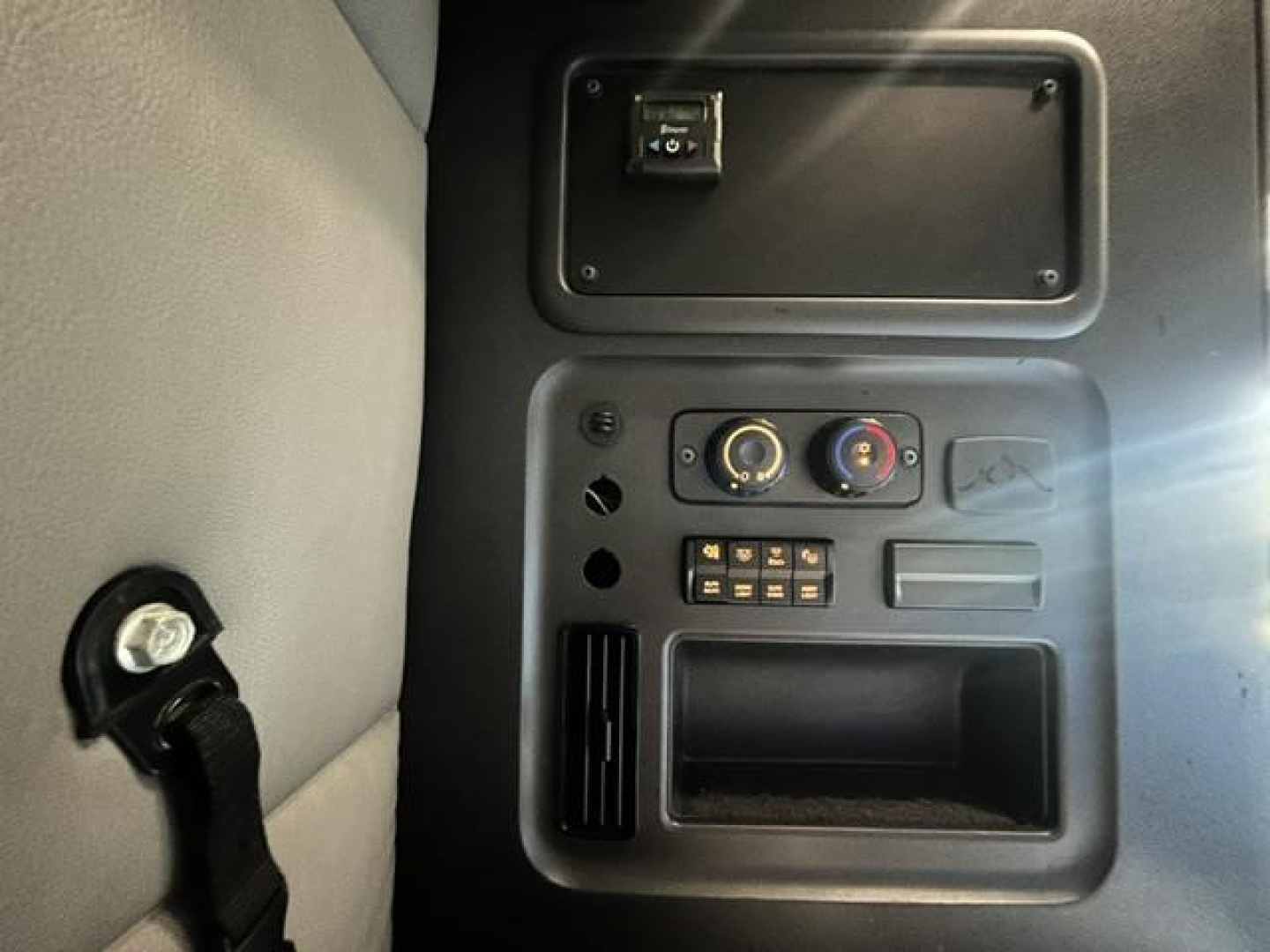 Cab interior panel of a Freightliner Cascadia showing a control panel with two circular gauges, a small keypad, vent, and storage pocket.