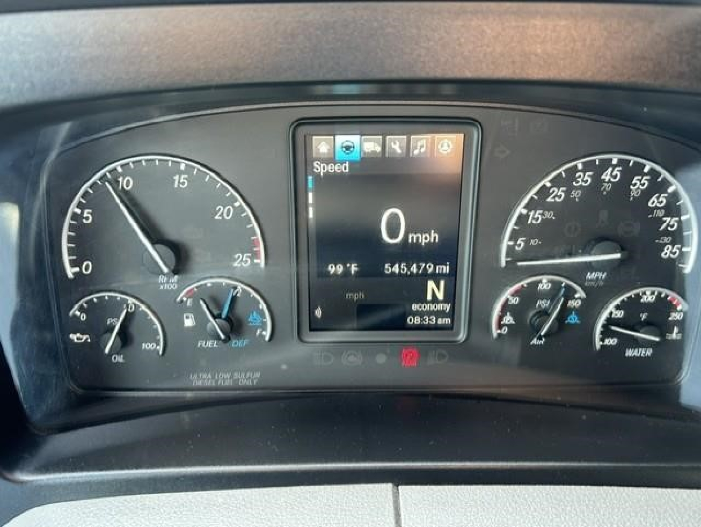 Vehicle dashboard of a Freightliner Cascadia showing digital speed readout at 0 mph, outside temp 99°F, odometer 545,479 mi, various gauges for fuel, oil, and water.