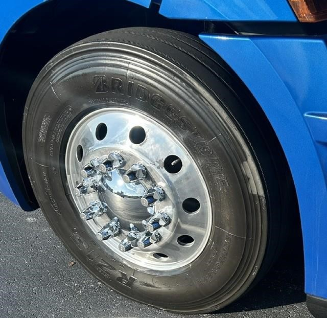 Bridgestone tire and front wheel of a blue 2022 Freightliner Cascadia 126 sleeper cab showing wheel, lug nuts, and wheel well.