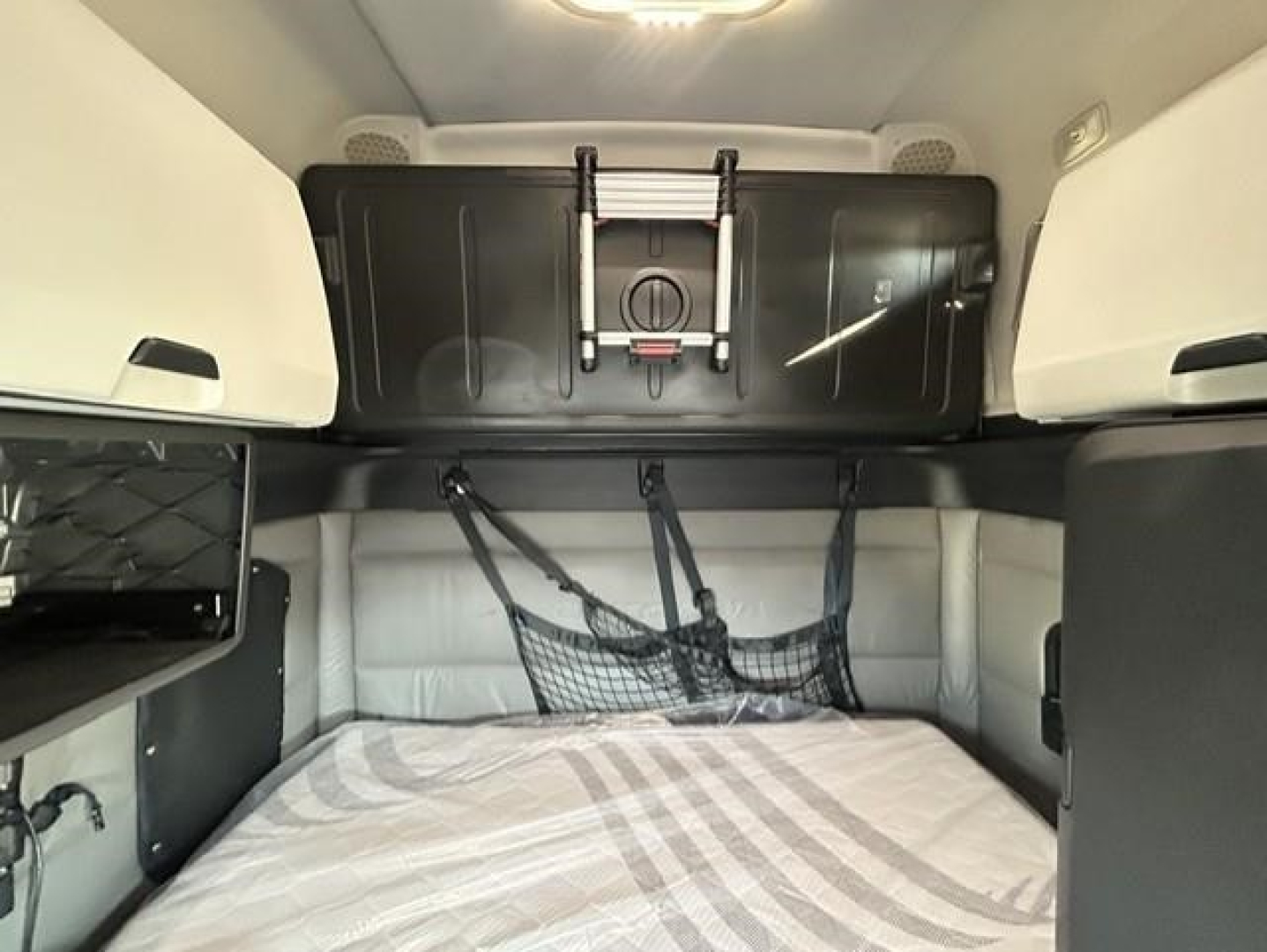 Freightliner Cascadia sleeper cab interior with bed, storage cabinet, and hanging net.