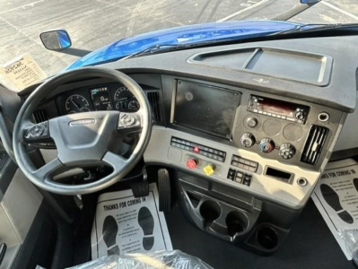 Dashboard of a Freightliner Cascadia 126 truck cab showing steering wheel, instrument cluster, center console with controls, and cup holders.