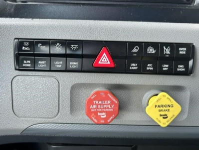 Freightliner Cascadia dash area showing control buttons, hazard switch, red trailer air supply knob, and yellow parking brake knob.