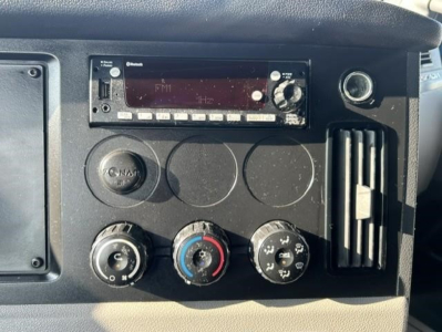 Truck dashboard showing radio unit, HVAC controls, and circular gauges with knobs in a Freightliner Cascadia interior.