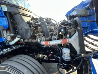 Freightliner Cascadia engine bay showing multiple hoses, coolant reservoir, air filter housing, and oil filter canister.