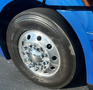 Bridgestone tire and front wheel of a blue 2022 Freightliner Cascadia 126 sleeper cab showing wheel, lug nuts, and wheel well.
