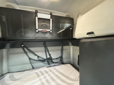 Freightliner Cascadia sleeper cab interior showing storage bunk area with hanging storage net and overhead cabinet.