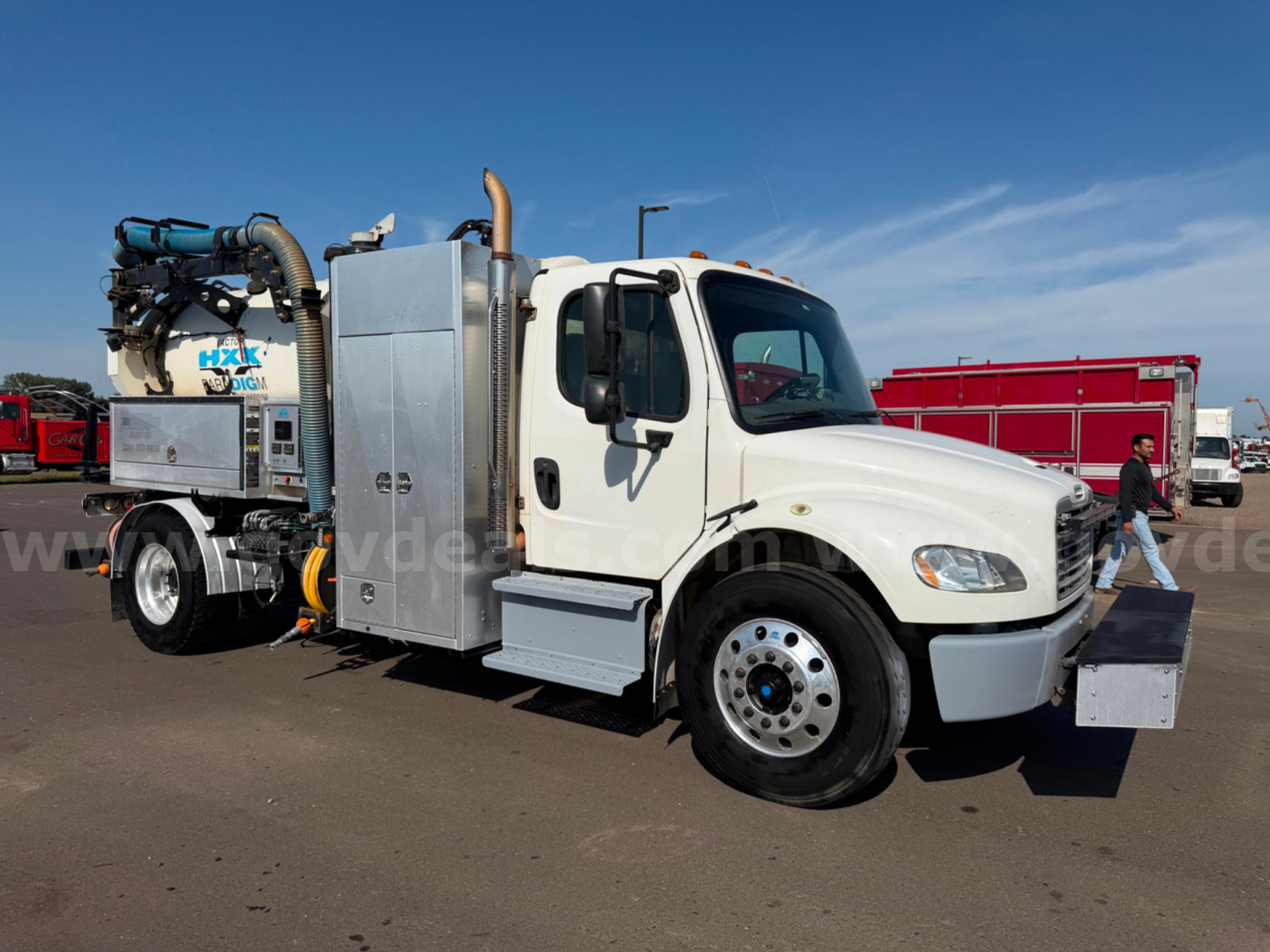 Freightliner Vactor vacuum truck side view showing vacuum hose assembly and metal utility compartments on a white cab chassis.