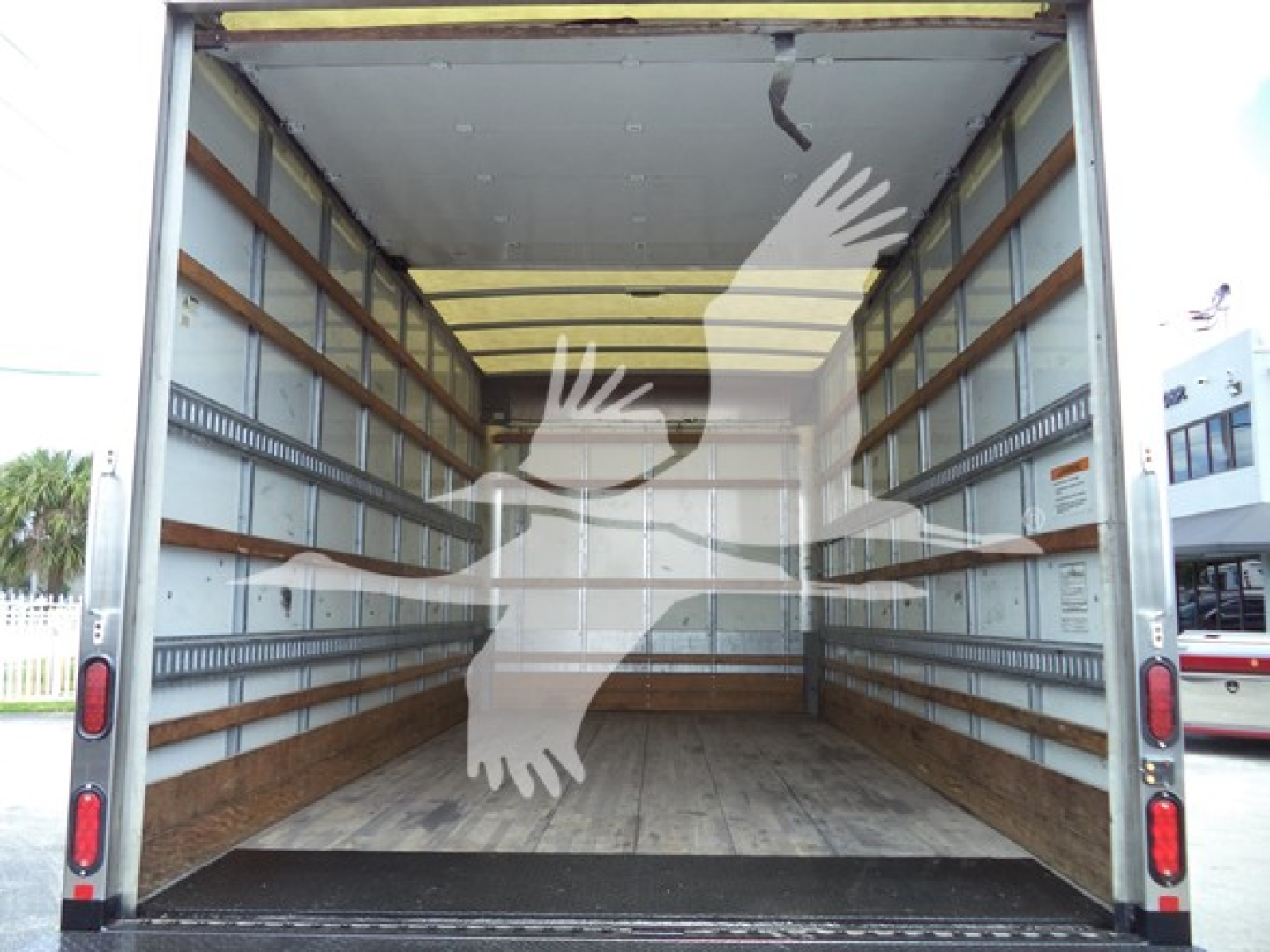 Isuzu NPR box truck cargo area interior showing empty plywood floor and metal side walls with rack rails; rear doors open.