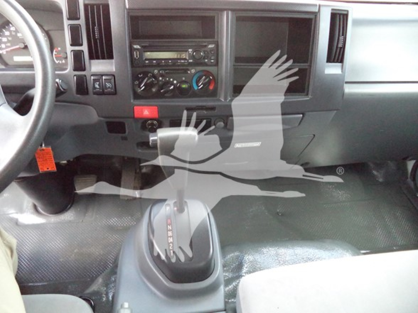 Isuzu NPR interior dashboard with center console, gear shift visible, steering wheel on left, controls and vents in view.