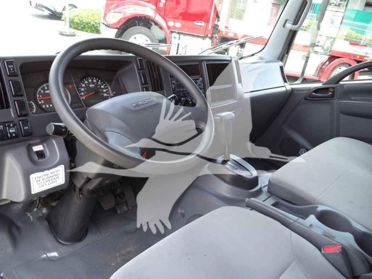 Isuzu NPR truck interior showing steering wheel, dashboard, and front seats with gear shifter; view through driver's side window.