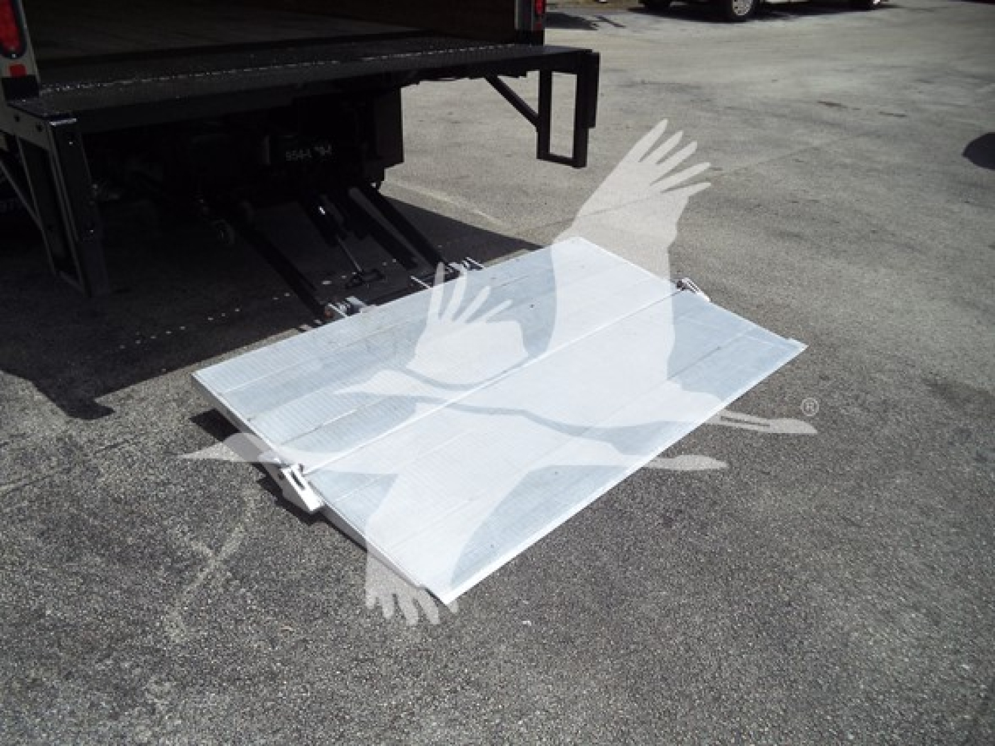 Isuzu NPR truck bed with fold-down aluminum ramp or platform near rear, visible reflective sheet metal and truck hitch area.