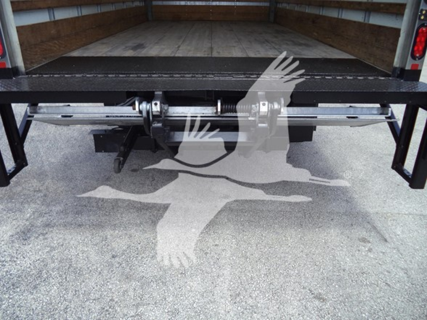 Isuzu NPR truck bed with hydraulic lift and undercarriage components visible in the cargo area.