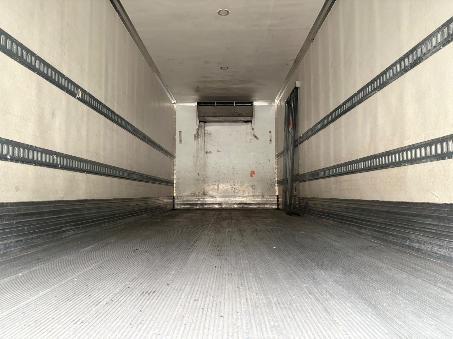 Truck trailer interior view showing empty cargo area with ribbed side rails and a rear loading door.