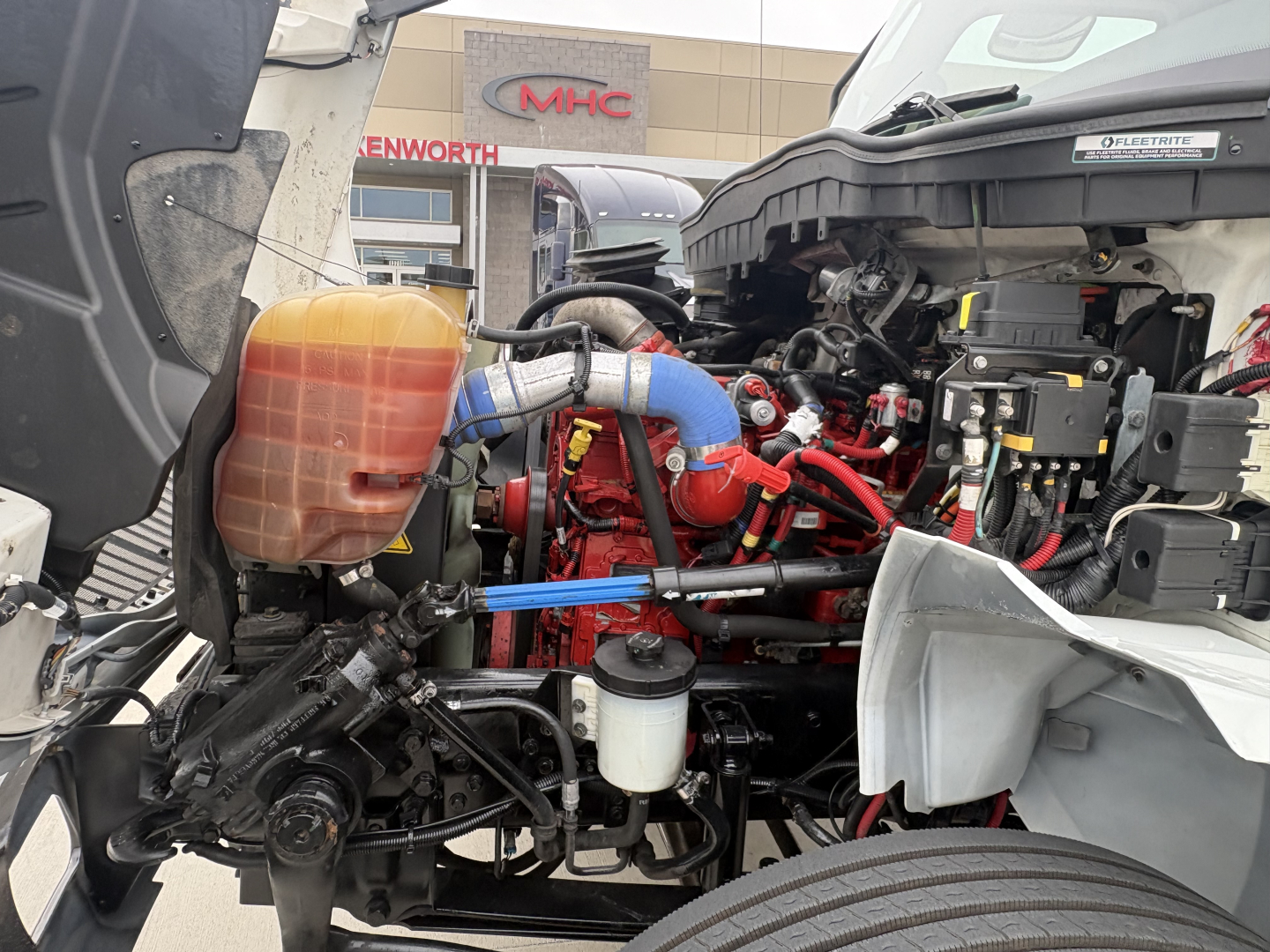 Engine bay of a 2020 International MV607 truck showing red engine, blue cooling hose, fluid reservoir, and surrounding components.