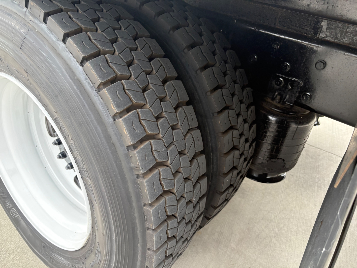 Front wheel twin tires and suspension area of a refrigerated 2020 International MV607 truck showing dual rear tires and undercarriage components.
