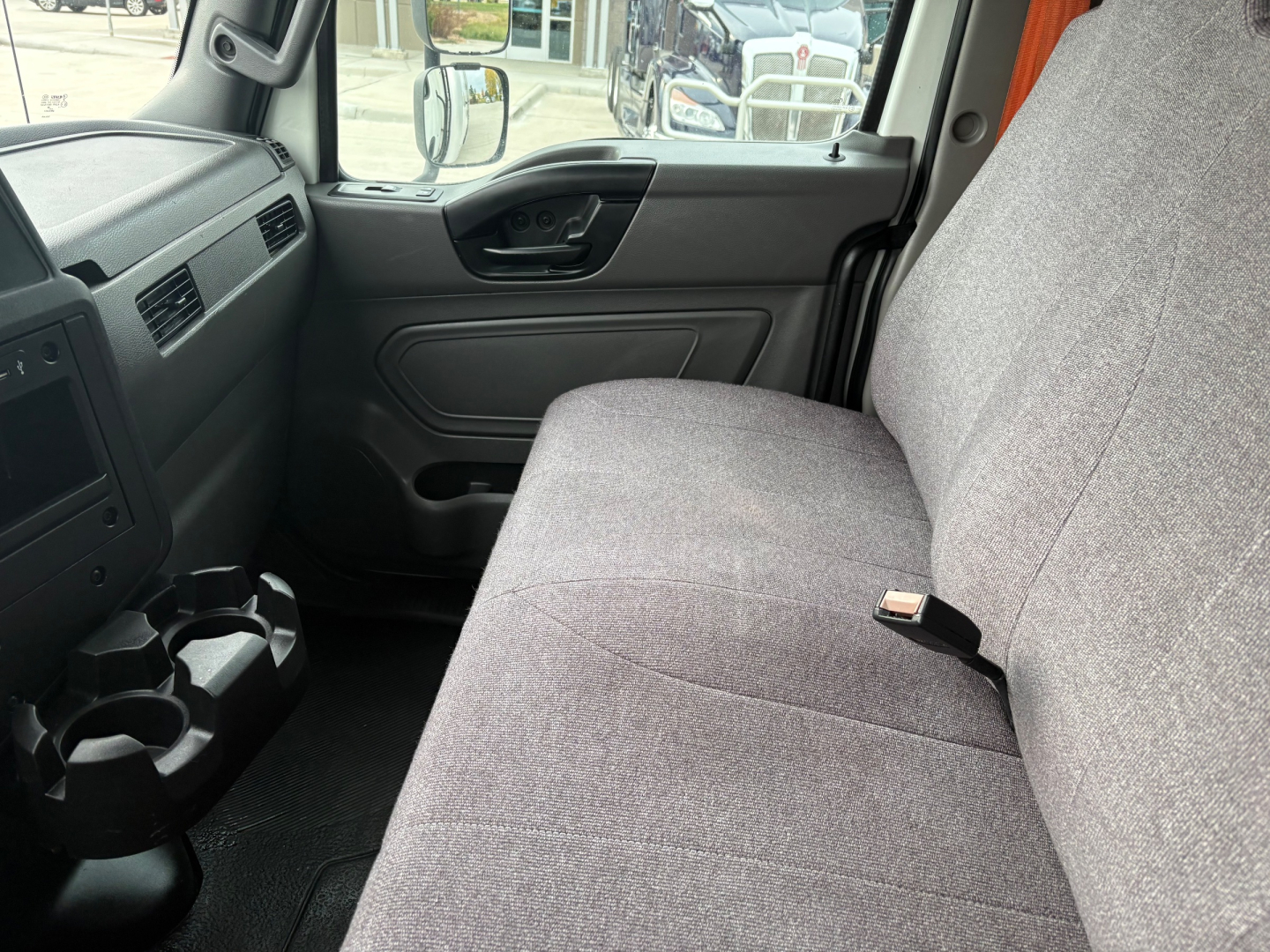 Truck interior front cabin with gray fabric bench seat, steering wheel, door panel, and center cup holders visible.