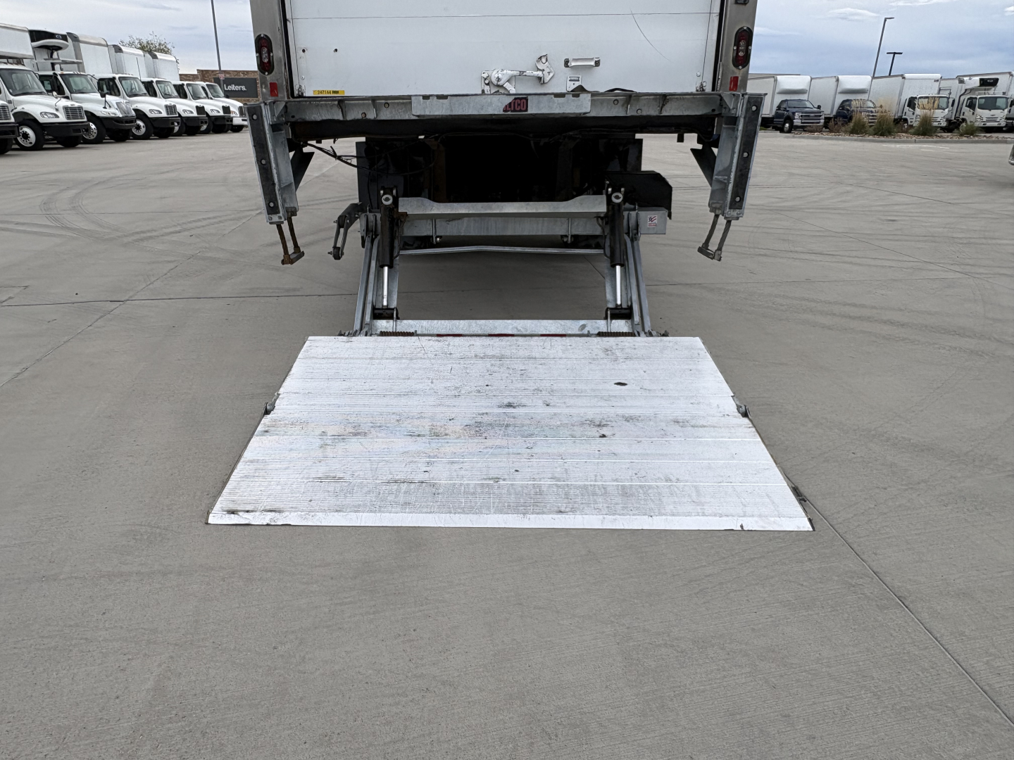 Rear view of a 2020 International MV607 refrigerated truck showing a lowered aluminum folding ramp extending from the rear cargo area.