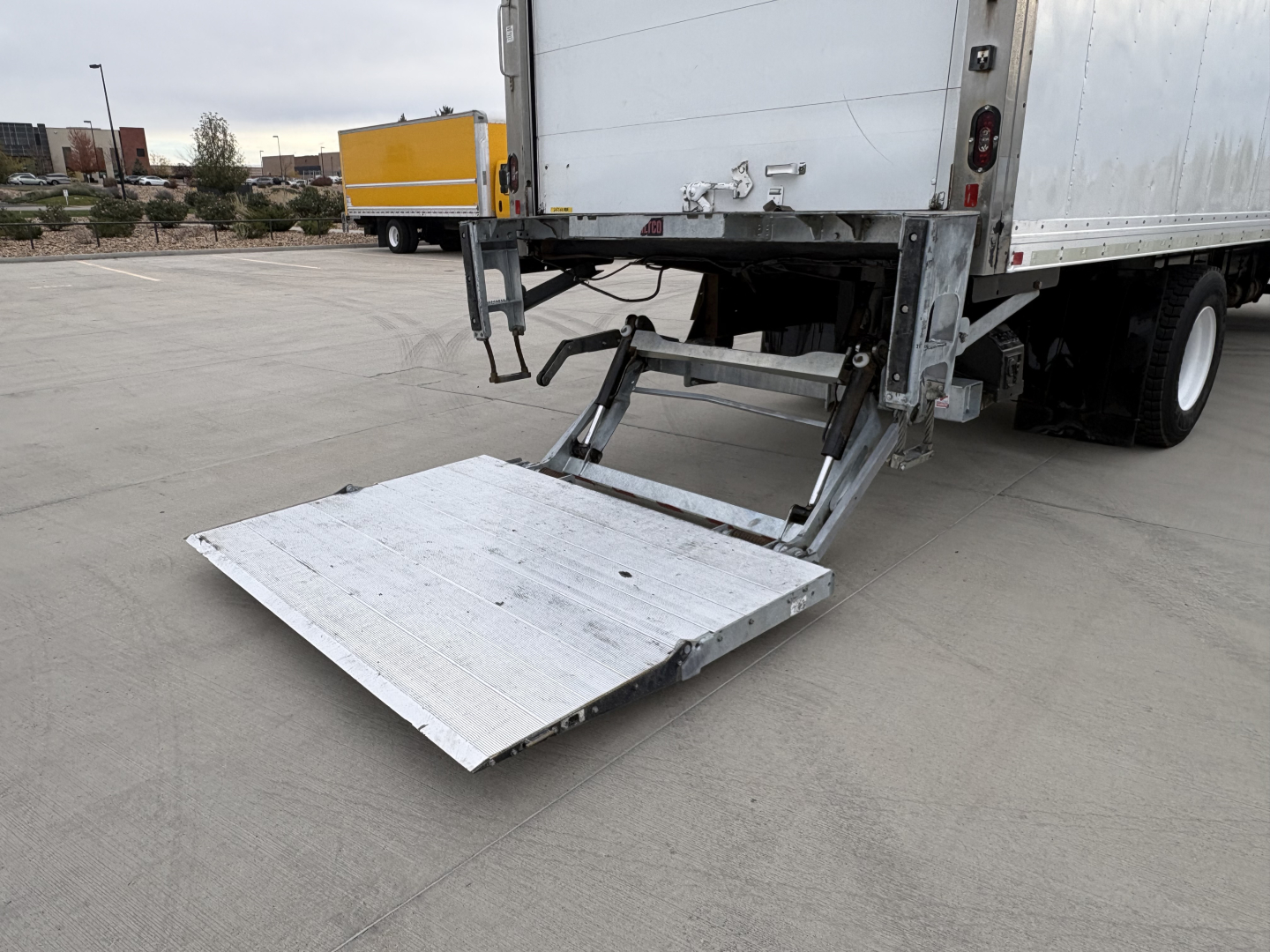 Truck tailgate lift platform extended showing aluminum ramp at rear of refrigerated semi-trailer.