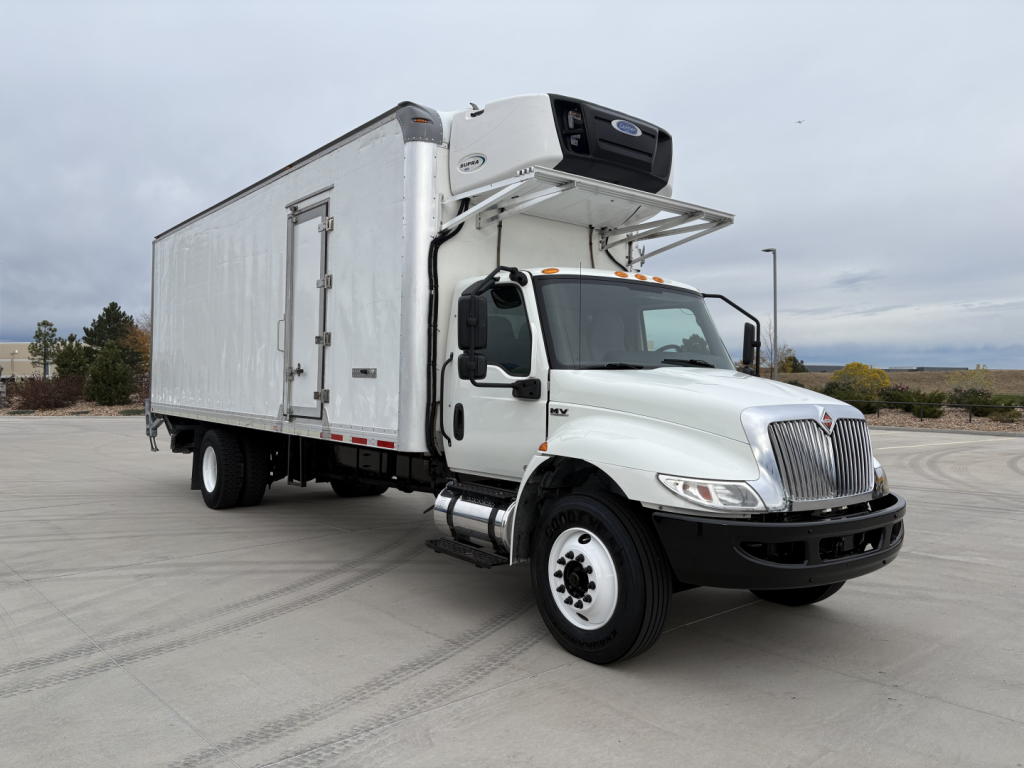Truck with a refrigerated box and a front-mounted refrigeration unit on a white International MV607 chassis; cab door visible, side access door on box, clean tire treads.