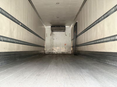 Truck trailer interior view showing empty cargo area with ribbed side rails and a rear loading door.