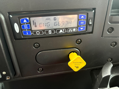 Vehicle cabin screen showing ENG 66334 and various control icons and a yellow parking brake key tag.
