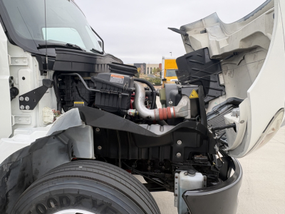 Truck engine bay of a 2020 International MV607 with hood open, showing cold storage refrigeration unit and engine components. Visible: radiator, hoses, and front wheel area.