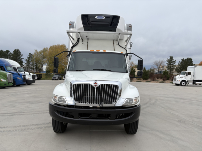 Front view of a white 2020 International MV607 refrigerated truck with a raised refrigeration unit above the cab, large grille, and black bumper.