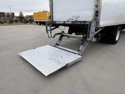 Truck tailgate lift platform extended showing aluminum ramp at rear of refrigerated semi-trailer.